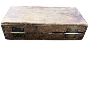 May include: A rectangular wooden box with a distressed finish. The box is closed, with visible hinges and a clasp. The wood has a weathered appearance, with variations in color and texture, suggesting age and use. The hinges are made of metal.