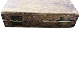 May include: A rectangular wooden box with a distressed finish. The box is closed, with visible hinges and a clasp. The wood has a weathered appearance, with variations in color and texture, suggesting age and use. The hinges are made of metal.