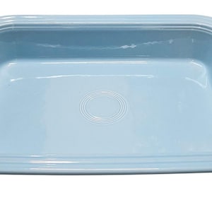 Może przedstawiać: Jasnoniebieskie prostokątne naczynie do pieczenia z zaokrągloną krawędzią i koncentrycznym wzorem okręgów pośrodku. Naczynie wykonane jest z ceramiki i ma około 30 cm długości i 20 cm szerokości.