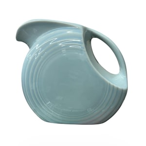 May include: A white ceramic mug with a black handle and the text "But First, Coffee" in a bold, black font. The mug is set against a blurred background, suggesting a cozy setting.