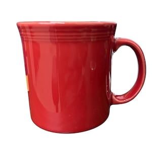 May include: A bright red ceramic mug with a rounded body and a large, curved handle. The mug has a glossy finish and a simple, classic design. The mug is approximately 10 cm tall.