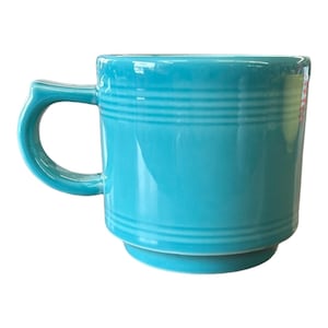 May include: A turquoise ceramic mug with a rounded handle. The mug has a cylindrical shape with horizontal ridges near the top and base. The mug is a solid, bright turquoise color.