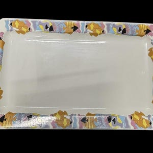 May include: Rectangular white serving tray with a decorative border. The border features a repeating pattern of stylized fish and abstract shapes in yellow, black, pink, and blue. The tray has rounded corners.