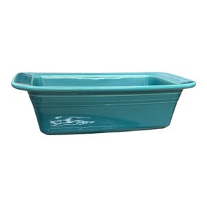 May include: A rectangular, turquoise ceramic baking dish with a slightly flared rim. The dish has a smooth, glossy finish and horizontal grooves along the sides. The interior is a solid turquoise color, and the dish is empty.