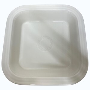 May include: A square, off-white ceramic dish with rounded corners. The dish has a slightly raised rim and a circular, concentric design in the center. The overall design is simple and clean, suitable for serving or display.