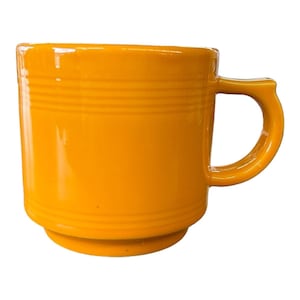 May include: A bright yellow ceramic mug with a rounded base and a curved handle. The mug features horizontal ridged detailing around the body. The glossy finish reflects light, highlighting the vibrant color. A classic, functional piece for enjoying hot beverages.