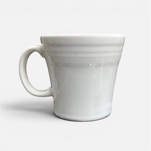 May include: A white ceramic mug with a curved handle. The mug has a slightly flared shape and horizontal ridges near the top. The mug is clean and glossy, with a simple, classic design.