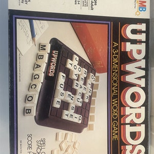 May include: A box for the board game Upwords, a 3-dimensional word game. The box is red, orange, and yellow with the game's name in large, bold letters. The box shows a close-up of the game board with letter tiles and a pencil.