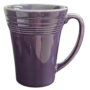 May include: A glossy, purple ceramic mug with a curved handle. The mug has a flared shape with horizontal ridged detailing around the upper portion. The mug is designed for hot beverages and is suitable for home or office use.