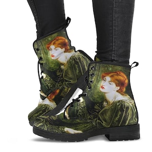 May include: Black lace-up boots featuring a Pre-Raphaelite painting of a woman with red hair and a green dress. The artwork is printed on the boots, which have a black sole and laces. The boots are worn with black pants.