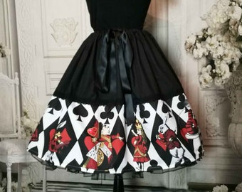 May include: A black skirt featuring a wide hem band with a white diamond pattern, black card suit symbols, and illustrations of characters including a queen and a rabbit. The skirt has a solid black upper section with a black ribbon tie at the waist.