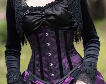 May include: A woman wearing a black velvet jacket with lace trim over a purple corset with black lace details. The corset has a satin ribbon and metal buttons.