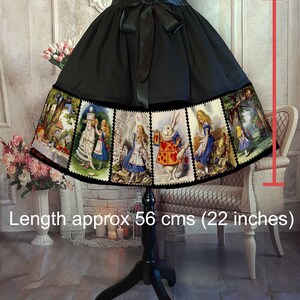 May include: A black skirt featuring a wide hem panel printed with multiple Alice in Wonderland illustrations in a stamp-like border. The skirt has a black satin ribbon tie at the waist and a length of approximately 22 inches as indicated by a red graphic.
