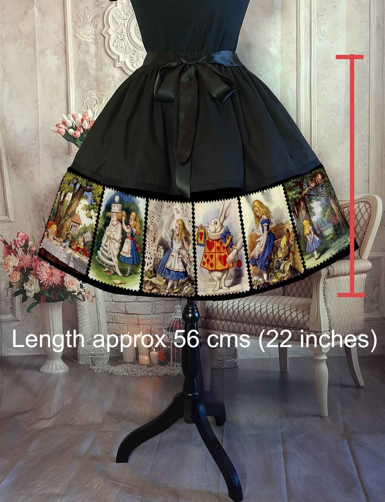 May include: A black skirt featuring a wide hem panel printed with multiple Alice in Wonderland illustrations in a stamp-like border. The skirt has a black satin ribbon tie at the waist and a length of approximately 22 inches as indicated by a red graphic.