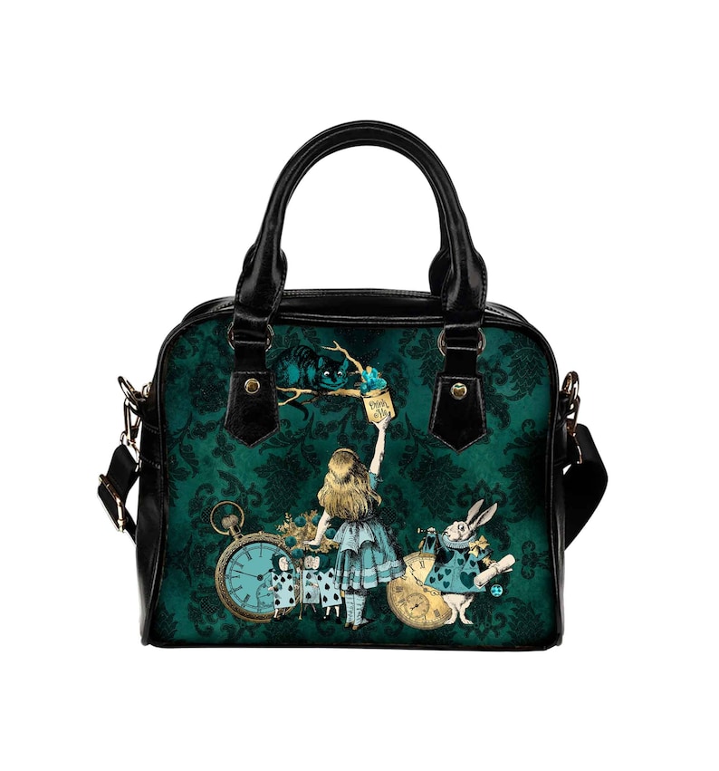 May include: A black and green handbag with a print of Alice in Wonderland characters. The print features Alice, the Cheshire Cat, the Mad Hatter, and the White Rabbit. The bag has a black strap and a top handle.