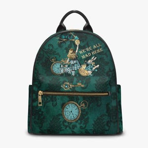 May include: A dark teal backpack featuring a black damask pattern and Alice in Wonderland illustrations. The bag displays the text WE'RE ALL MAD HERE, a pocket with a gold key, and a pocket watch graphic. It has black trim and a top handle.