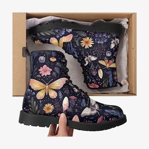 May include: A pair of black combat boots with a dark blue floral and butterfly pattern. The boots are in a cardboard box with tissue paper. The boots have black laces and soles. The butterfly wings are yellow and orange.