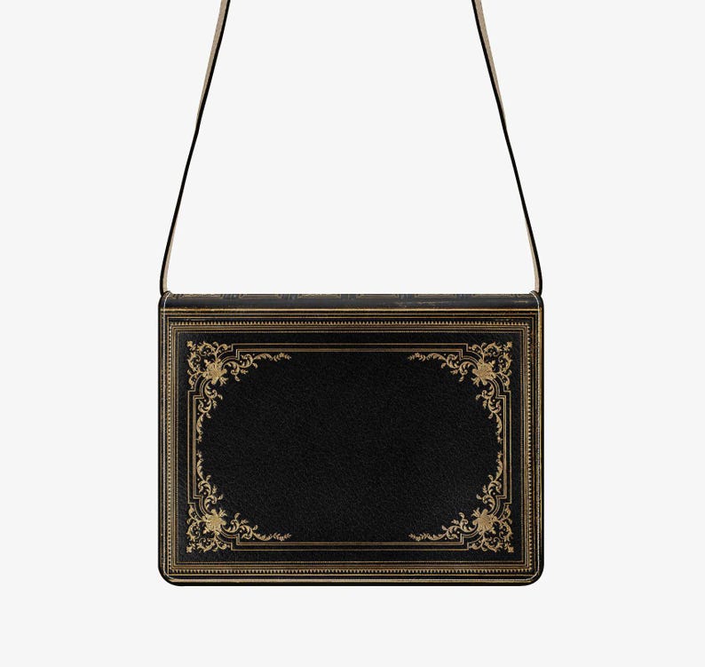 K&ouml;nnte beinhalten: Eine schwarze Umh&auml;ngetasche, die wie ein antikes Buch gestaltet ist. Die Tasche hat goldfarbene, verzierte Details an den R&auml;ndern und einen passenden Riemen. Die rechteckige Form und das klassische Design der Tasche wirken zeitlos elegant.