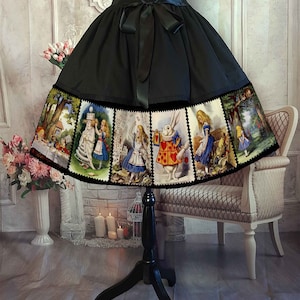 May include: A black skirt featuring a wide hem border printed with multiple rectangular panels depicting scenes from Alice in Wonderland, including characters like the White Rabbit and Alice. The skirt has a black satin ribbon tied at the waist.