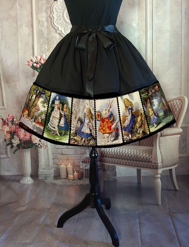 May include: A black skirt featuring a wide hem border printed with multiple rectangular panels depicting scenes from Alice in Wonderland, including characters like the White Rabbit and Alice. The skirt has a black satin ribbon tied at the waist.