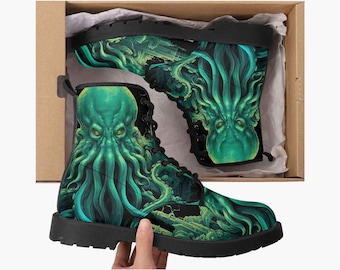 May include: A pair of black lace-up boots featuring a vibrant green and teal graphic print of a tentacled creature. One boot is displayed inside a cardboard box, while the other is held up, showcasing the detailed aquatic monster design.