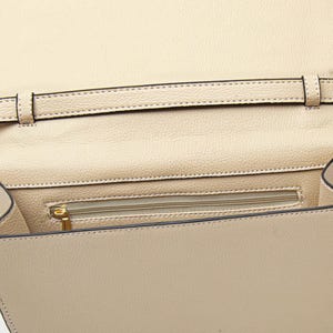 K&ouml;nnte beinhalten: Beige Lederhandtasche mit Klappenverschluss. Der Innenraum verf&uuml;gt &uuml;ber eine Rei&szlig;verschlusstasche und einen Riemen. Die Tasche hat eine strukturierte Oberfl&auml;che und einen goldfarbenen Rei&szlig;verschluss. Die N&auml;hte sind an den Kanten und am Riemen sichtbar.