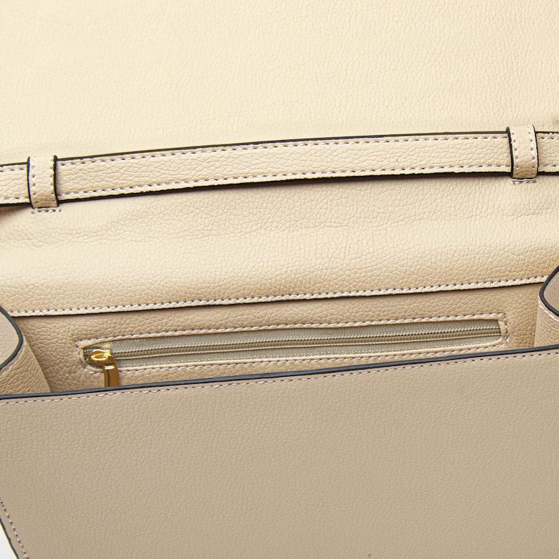 K&ouml;nnte beinhalten: Beige Lederhandtasche mit Klappenverschluss. Der Innenraum verf&uuml;gt &uuml;ber eine Rei&szlig;verschlusstasche und einen Riemen. Die Tasche hat eine strukturierte Oberfl&auml;che und einen goldfarbenen Rei&szlig;verschluss. Die N&auml;hte sind an den Kanten und am Riemen sichtbar.
