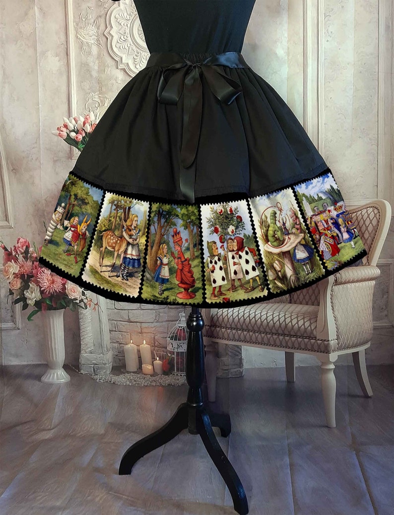 May include: A black skirt featuring a wide hem panel decorated with a series of rectangular illustrations depicting scenes from Alice in Wonderland, including characters like the Queen of Hearts and the Caterpillar, finished with a black waist ribbon.