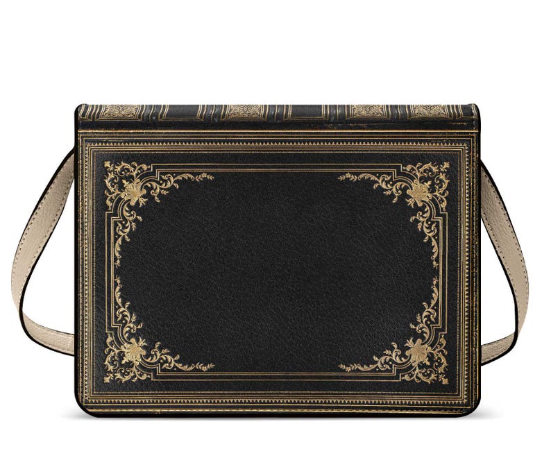K&ouml;nnte beinhalten: Schwarze Umh&auml;ngetasche im Design eines Vintage-Buches. Die Tasche hat goldfarbene, verzierte Eckdesigns und Verzierungen auf einem schwarzen, leder&auml;hnlichen Material. Sie hat einen beigefarbenen Schulterriemen und eine rechteckige Form.