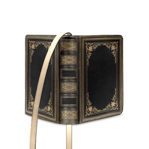 K&ouml;nnte beinhalten: Schwarze Handtasche, die wie ein offenes Buch gestaltet ist. Die Tasche hat goldfarbene Zierakzente und einen cremefarbenen Schulterriemen. Die buchf&ouml;rmige Tasche hat eine klassische, Vintage-&Auml;sthetik.