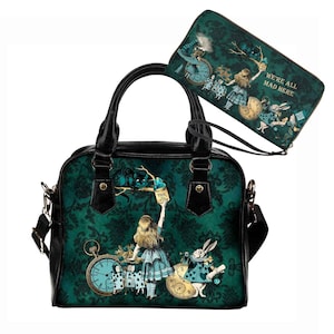 May include: A black handbag with a green and gold Alice in Wonderland themed print. The print features Alice, the Cheshire Cat, the White Rabbit, and a pocket watch. The handbag has a top handle and a shoulder strap. The matching wallet has the same print and the text "We're all mad here".