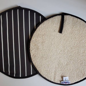 May include: Two round pot holders, one black with white stripes and one beige with a textured surface. Both have black trim and a loop for hanging.