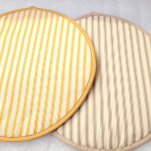 May include: Two round, striped fabric pot holders. One is yellow and white with a yellow border, the other is beige and white with a beige border. These pot holders are likely for kitchen use.