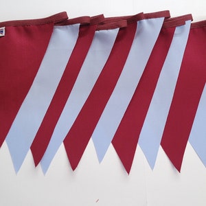 May include: A string of bunting flags with alternating burgundy and light blue panels. The flags are sewn together and have a small tag with the text "Made in Britain".