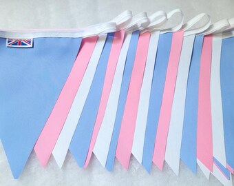 May include: A string of colorful triangular flags in light blue, pink, and white, connected by a white ribbon. The flags are arranged in a row, with a small Union Jack tag visible on one flag. The bunting is suitable for celebrations.