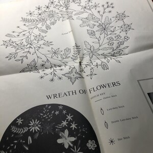 May include: A white paper embroidery pattern featuring a black line drawing of a floral wreath. The text reads WREATH OF FLOWERS and includes a STITCH KEY with symbols for Outline Stitch, Lazy-daisy Stitch, Double Lazy-daisy Stitch, and Star Stitch.