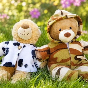 Puede incluir: Dos osos de peluche sentados uno al lado del otro. El oso de la izquierda lleva una chaqueta blanca con manchas negras de vaca y un botón marrón. El oso de la derecha lleva un mono con capucha de camuflaje en tonos marrón, verde y beige.