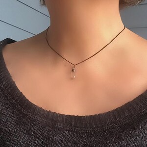 May include: A simple, delicate necklace with a clear crystal pendant hanging from a brown cord.