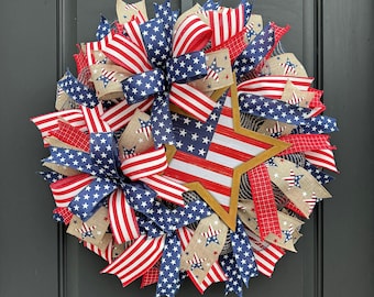 May include: A patriotic wreath with red, white, and blue ribbon and a large star in the center. The wreath is made of burlap and mesh.