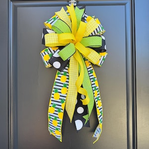 May include: A yellow, green, and black bow with pineapple and polka dot patterned ribbons. The bow is tied with a loop and tails.