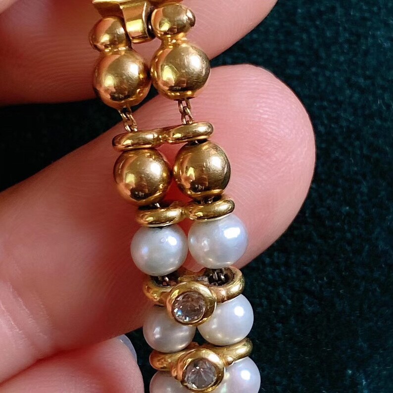 Op de afbeelding: Een gouden en parel armband met een sluiting. De armband heeft afwisselende gouden kralen en witte parels.