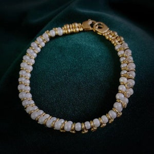 Op de afbeelding: Een gouden en witte parel armband met een sluiting. De armband heeft afwisselende gouden kralen en witte parels.