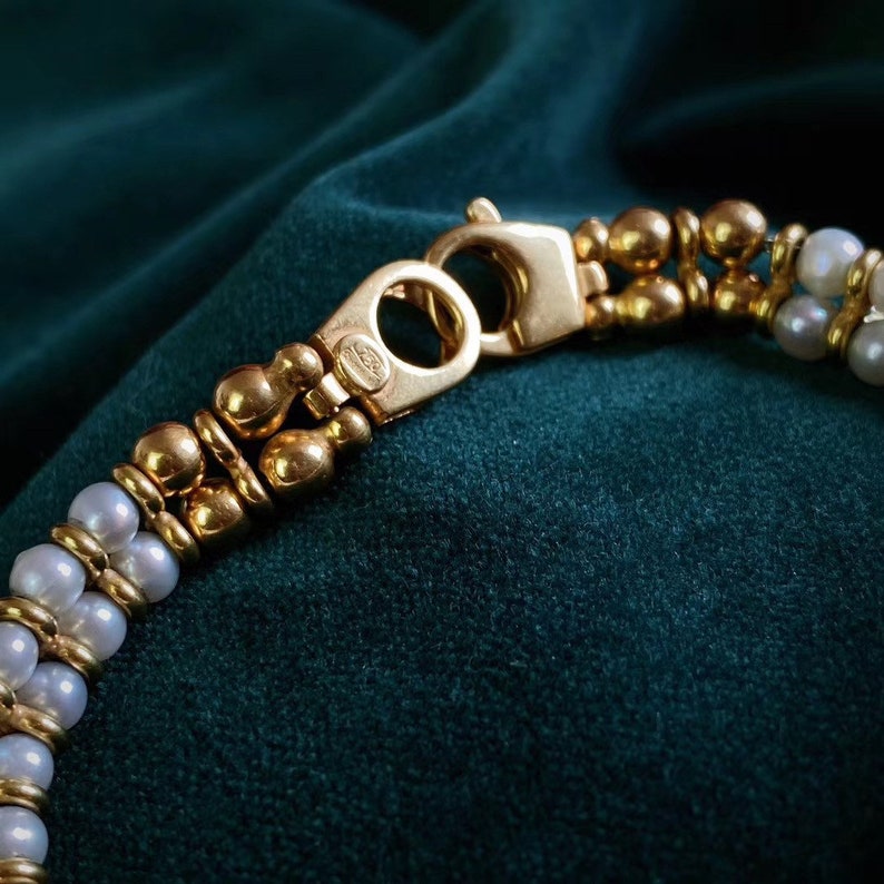 Op de afbeelding: Een gouden en parel armband met een sluiting. De armband is gemaakt van kleine gouden kralen en parels.