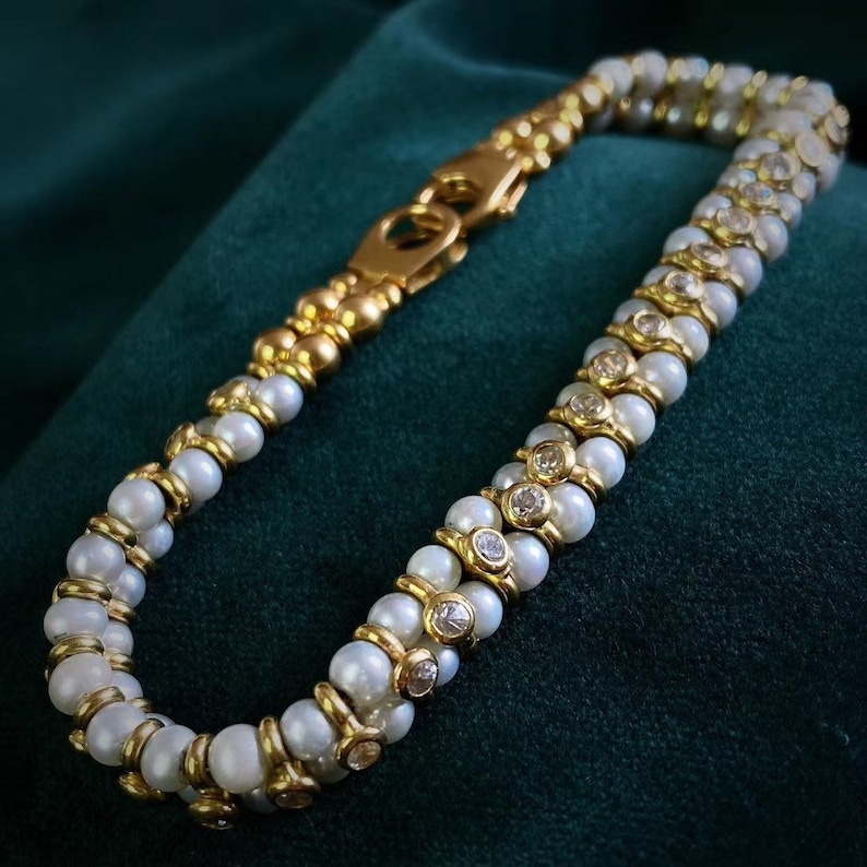 Op de afbeelding: Een gouden en witte parel armband met een dubbele rij parels en kleine diamanten. De armband heeft een gouden sluiting.