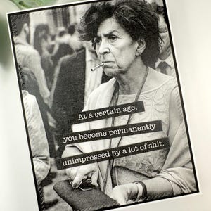 May include: Black and white art print featuring a woman with a cigarette, with the text "At a certain age, you become permanently unimpressed by a lot of shit." The image has a vintage, slightly grainy aesthetic.