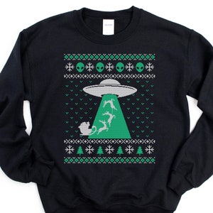 May include: Black sweatshirt with a green and white holiday design. The design features a UFO beaming up Santa's sleigh and reindeer. The top of the sweatshirt has a pattern of green alien heads and snowflakes.