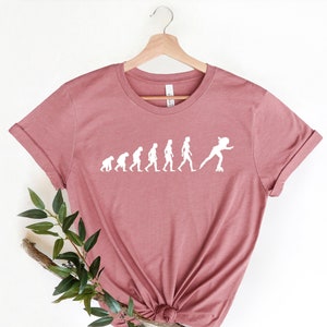 May include: A mauve t-shirt with a white graphic of the evolution of humans ending with a person roller skating. The graphic says "Evolution of a Roller Skater".