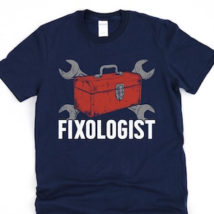 May include: Navy blue t-shirt with a red toolbox and crossed wrenches graphic. The word "FIXOLOGIST" is printed in white below the toolbox. The design is a humorous take on a repair person.