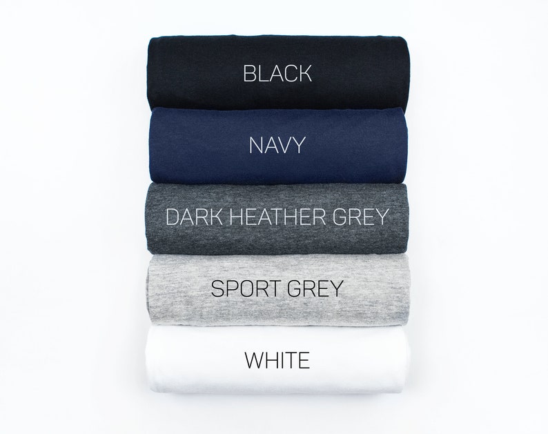 May include: Five rolled up t-shirts in different colors: black, navy, dark heather grey, sport grey, and white. The colors are labeled on each t-shirt.