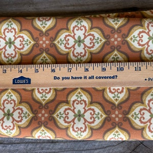 May include: Folded fabric featuring a repeating floral pattern in brown, cream, yellow, and green. A wooden ruler with centimetre markings and the text "Do you have it all covered?" is placed on top of the fabric.